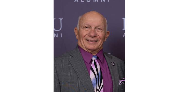  Carl Inzerillo, DO (COM 1964) smiles in a grey suit and purple tie. 